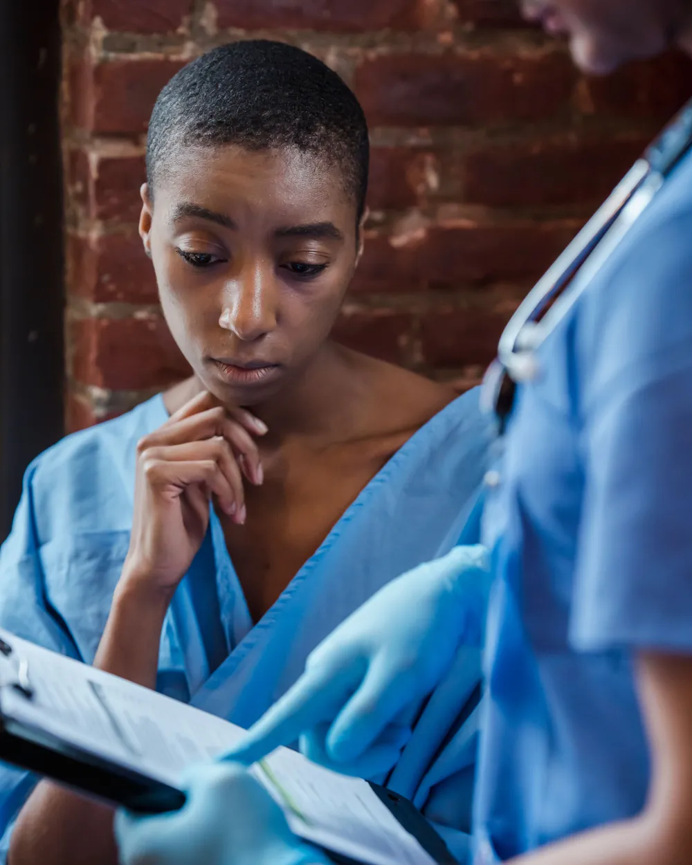 Patiente inquiète, en blouse d’hôpital, face à un document médical qu’un soignant lui présente